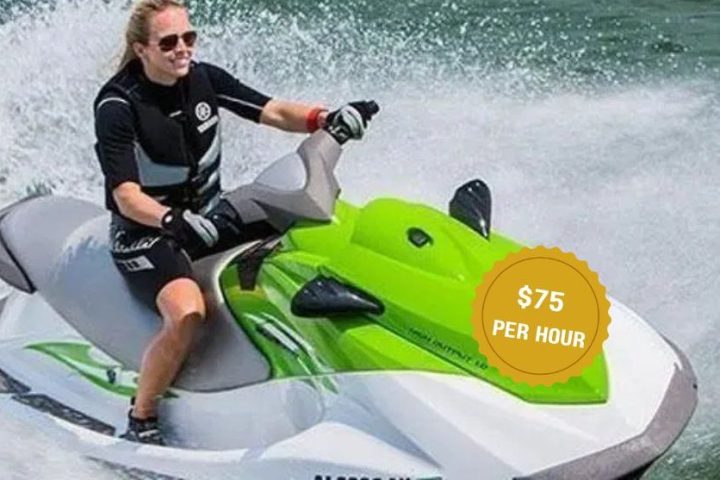 Person riding a green and white jet ski on water, wearing sunglasses.